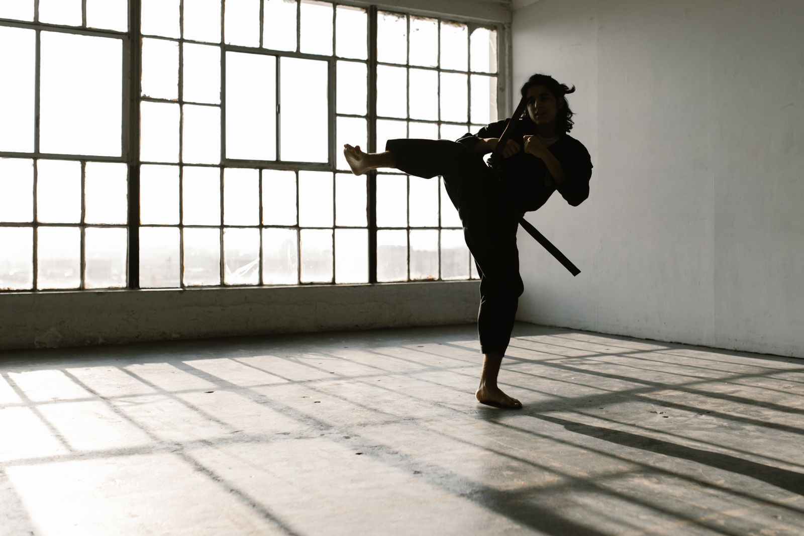 A martial artist performing a high kick, silhouetted against bright windows